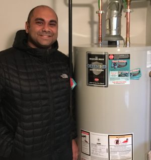A person in a black jacket stands indoors next to a Bradford White water heater.