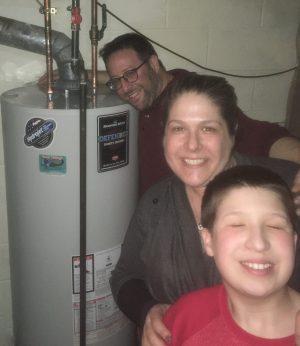 Three people smile and pose next to a water heater in a basement.