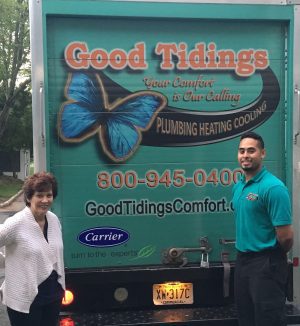 Two people stand by the back of a Good Tidings Plumbing Heating Cooling truck, which features a butterfly graphic and contact information.
