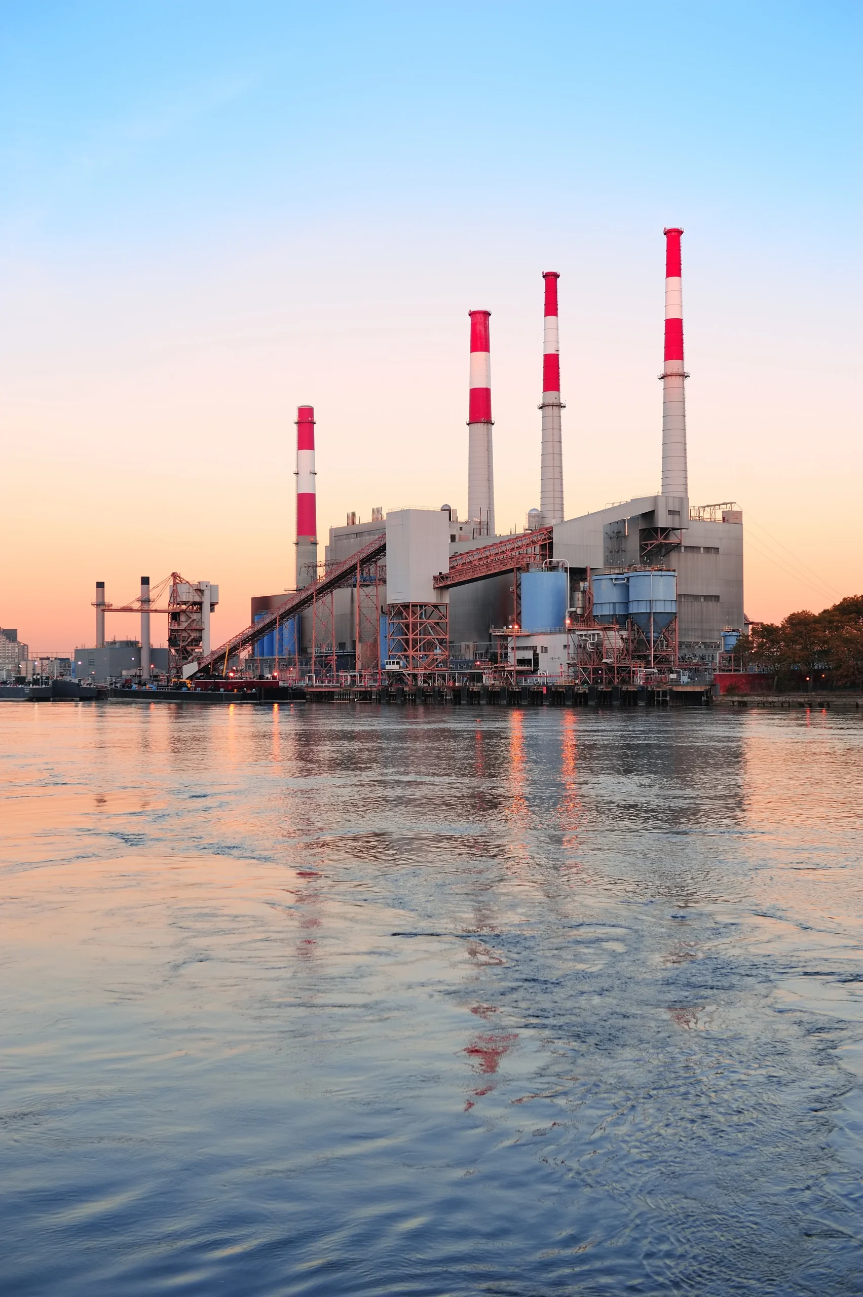 Power plant with smokestacks over water at sunset.