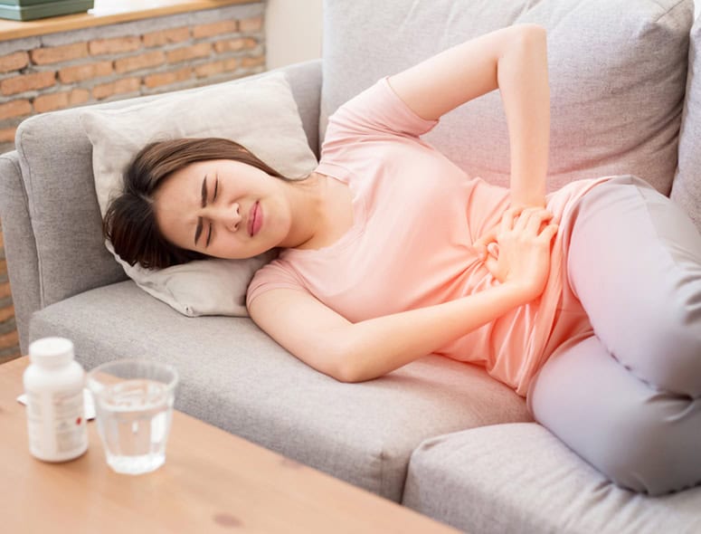 Young woman experiencing stomach pain on sofa at home.