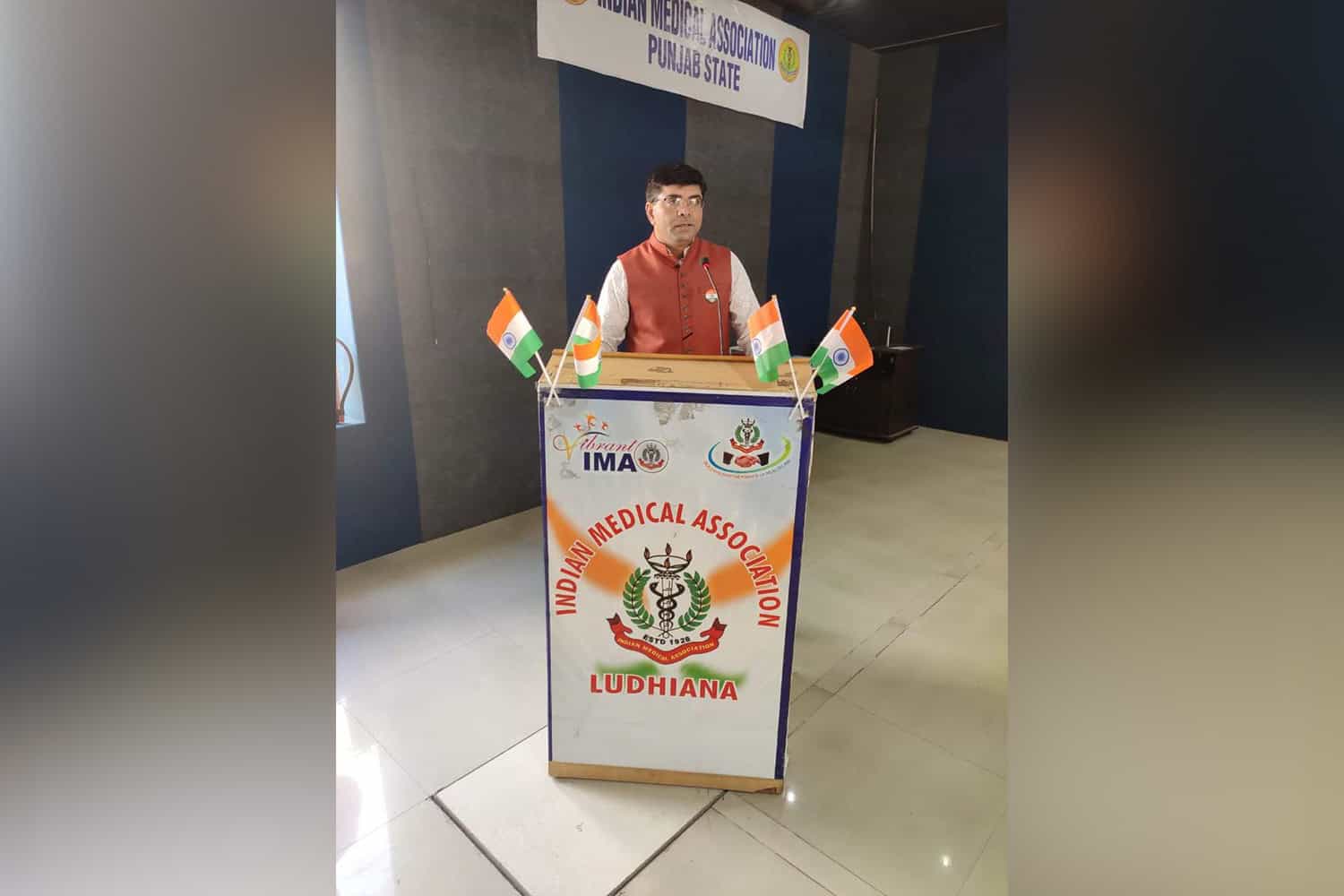 Man standing at a podium with Indian flags at a medical conference.