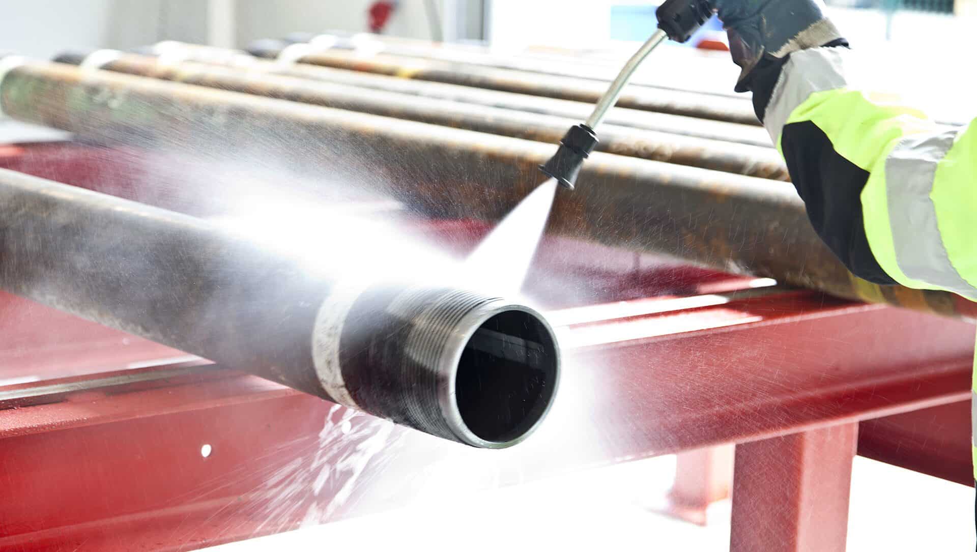 Wasserhöchstdruckstrahl reinigt verschmutztes Metallrohr, Wasserstrahl trifft auf die Oberfläche.