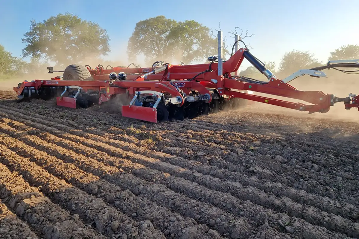 Large red cultivator tilling farmland in sunshine.