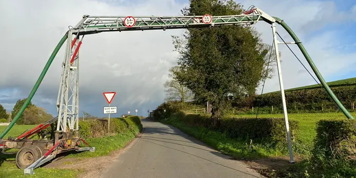 Narrow road with farm irrigation equipment overhead.