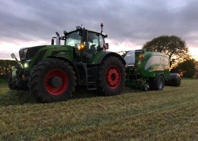 Tractor baling hay at sunset in field.