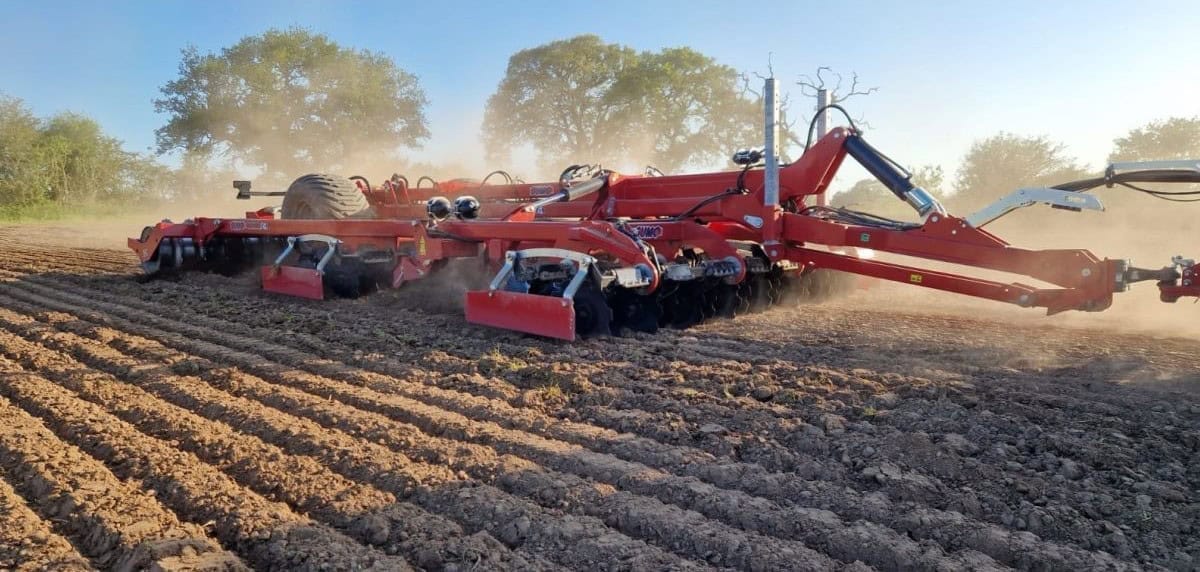 Red agricultural machinery cultivating a field.