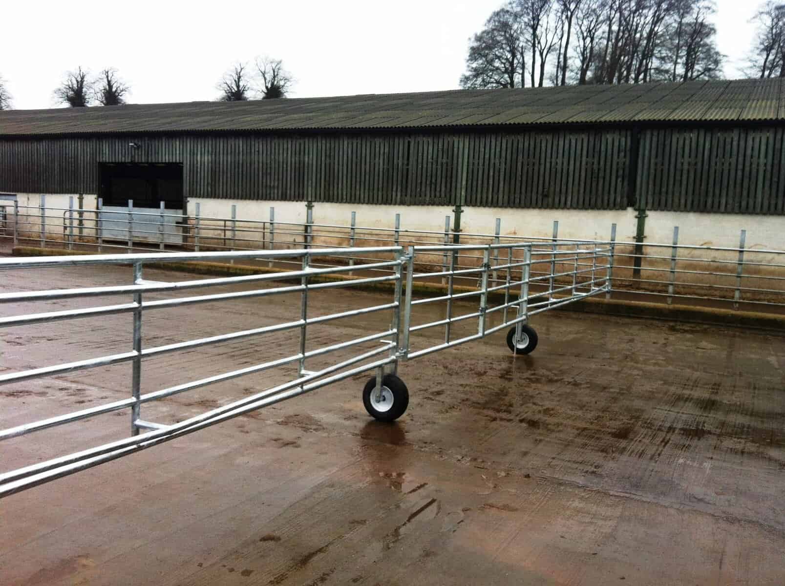 Metal livestock gates on wheels near a barn.