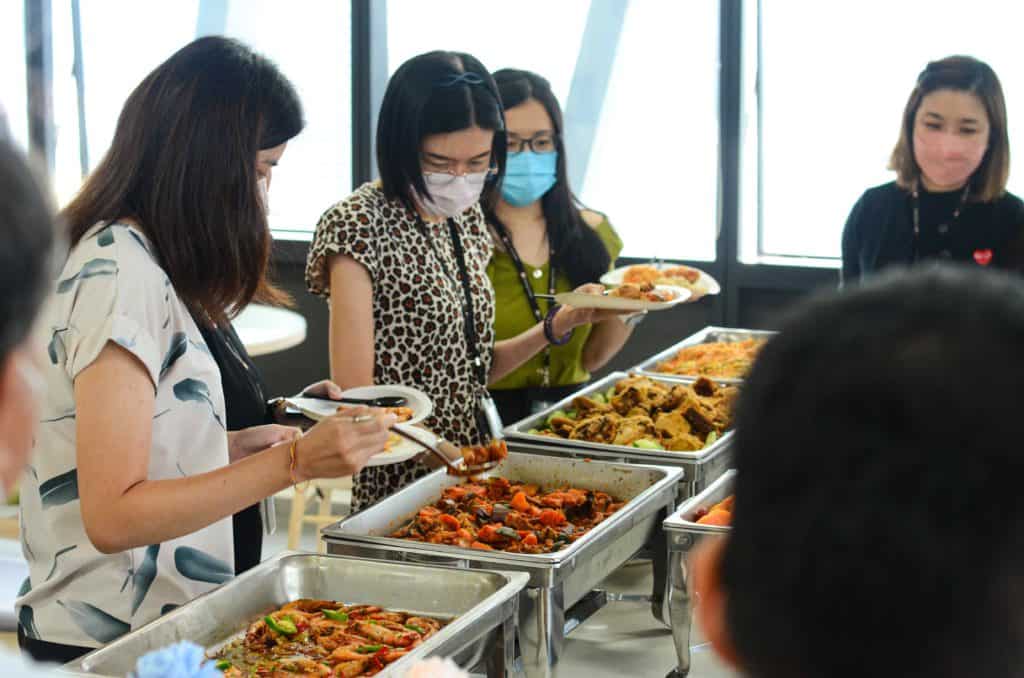 Guests wearing masks and getting food from silver trays at the office buffet catering by idocatering during 2022 COVID-19 pandemic