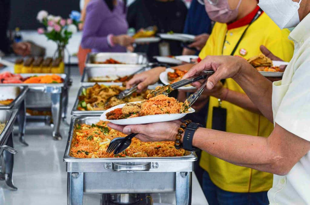 Guests wearing masks and getting food from silver trays at the office buffet catering by idocatering during 2022 COVID-19 pandemic 5