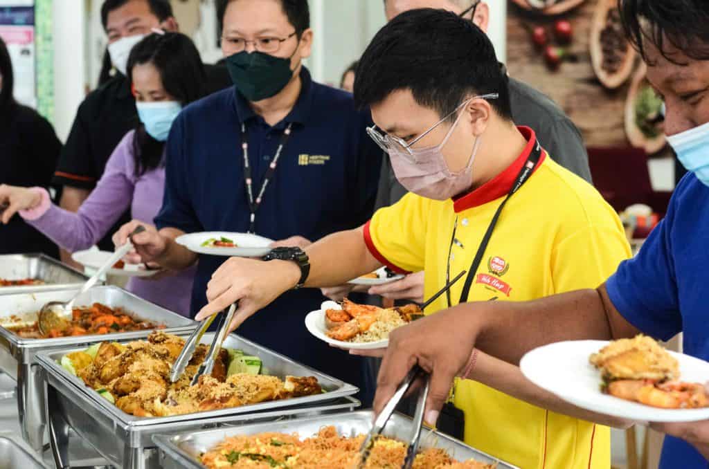 Yellow shirt guy wearing mask and getting food from silver trays at the office buffet catering by idocatering during 2022 COVID-19 pandemic 4