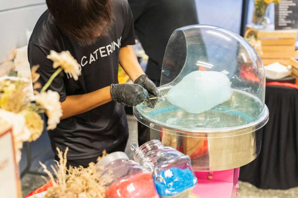 idocatering staff making blue candy floss using cotton candy machine at event catering booth