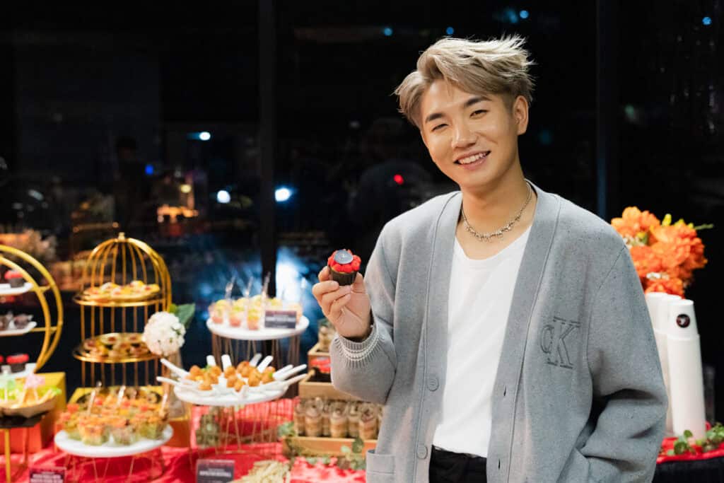 Guest KOL Chang Le smiling brightly showcasing red dessert cup cake from iDoCatering 
