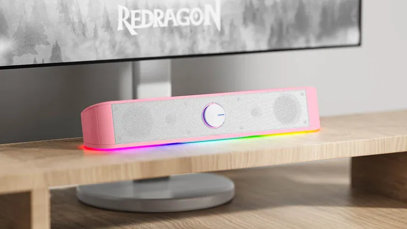 White Redragon GS560 soundbar with its RGB strip lit, under a monitor on a wooden desk