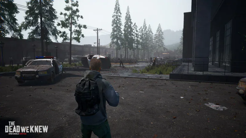 A survivor faces zombies on an abandoned town street beside a wrecked police car in The Dead We Knew