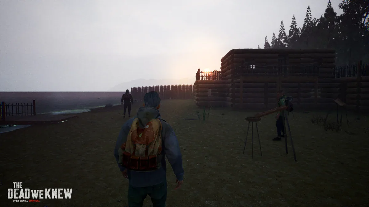 A survivor with a backpack walks towards a fenced log-cabin base at dusk while zombies close in, in The Dead We Knew
