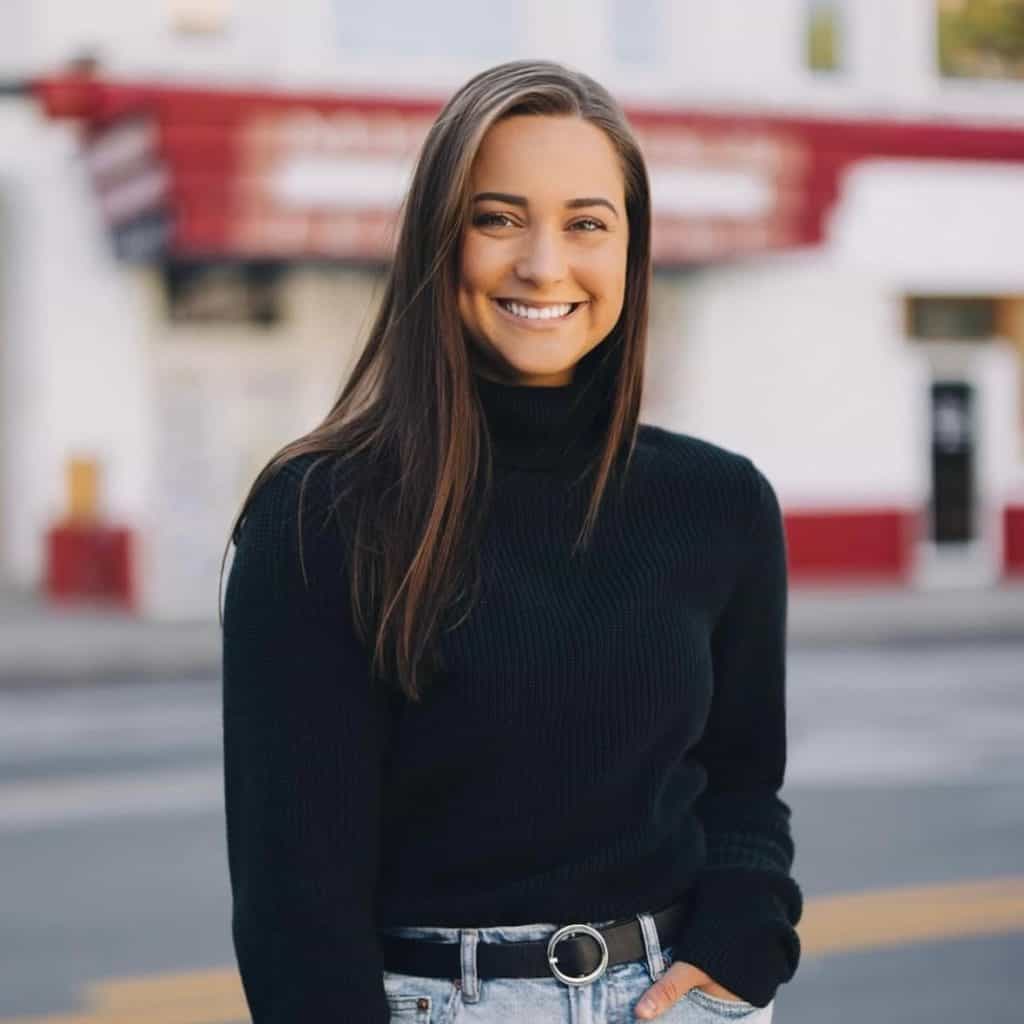 Smiling young woman in black sweater outdoors in front of a building.