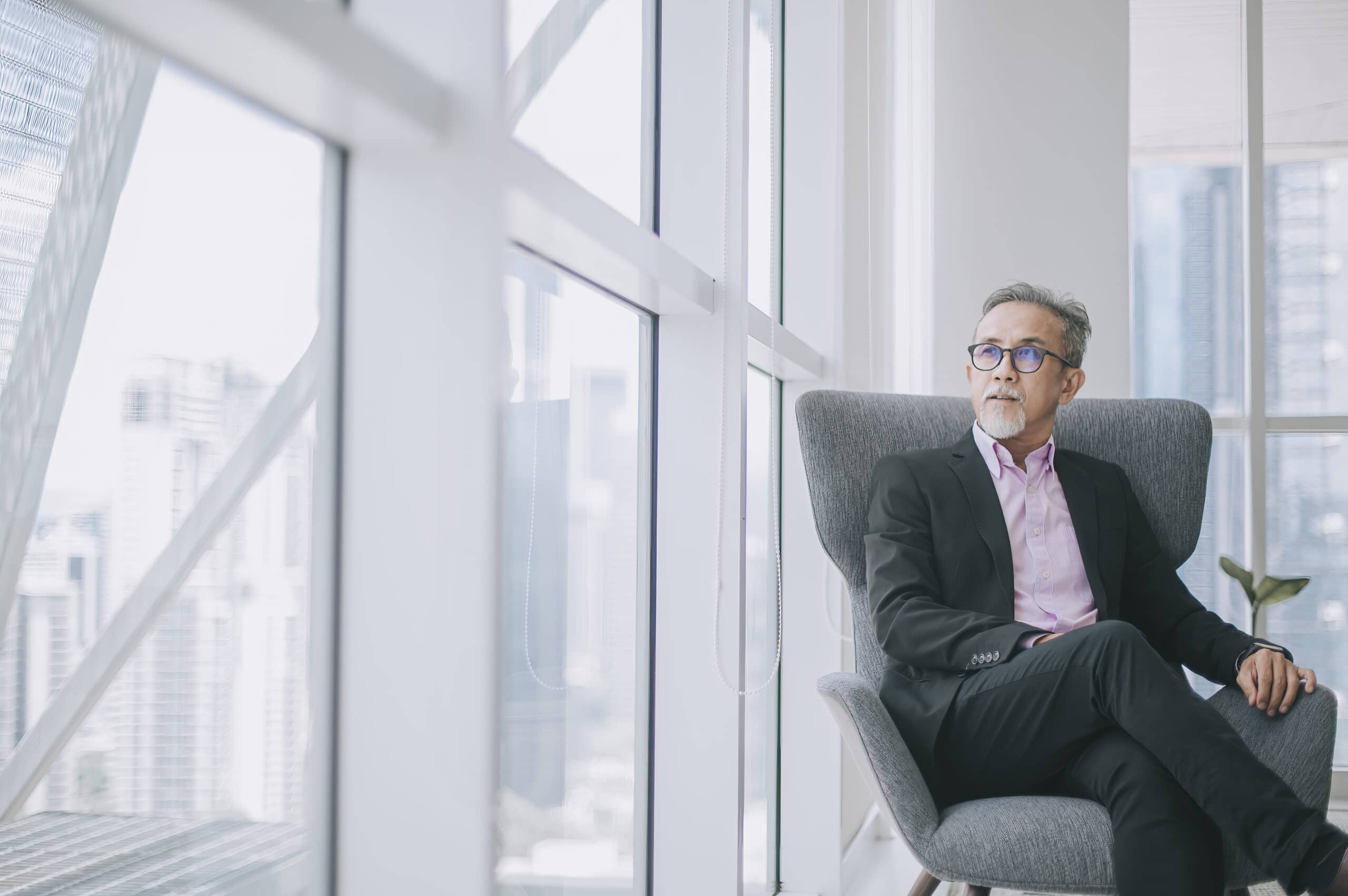 Professional executive seated by large windows in modern office, symbolizing independence and business success.