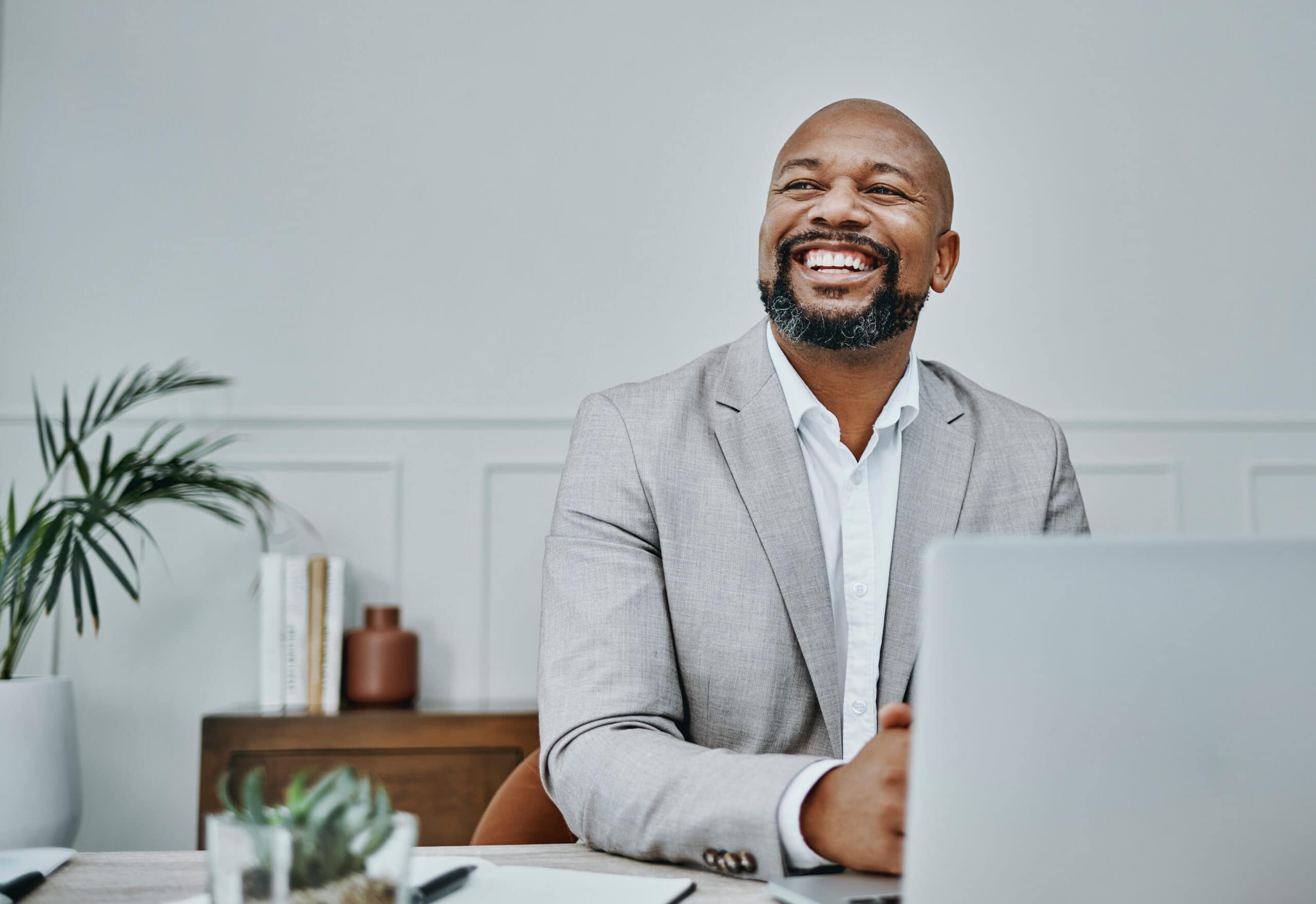 Diverse professional man working remotely smiling at laptop in modern office.