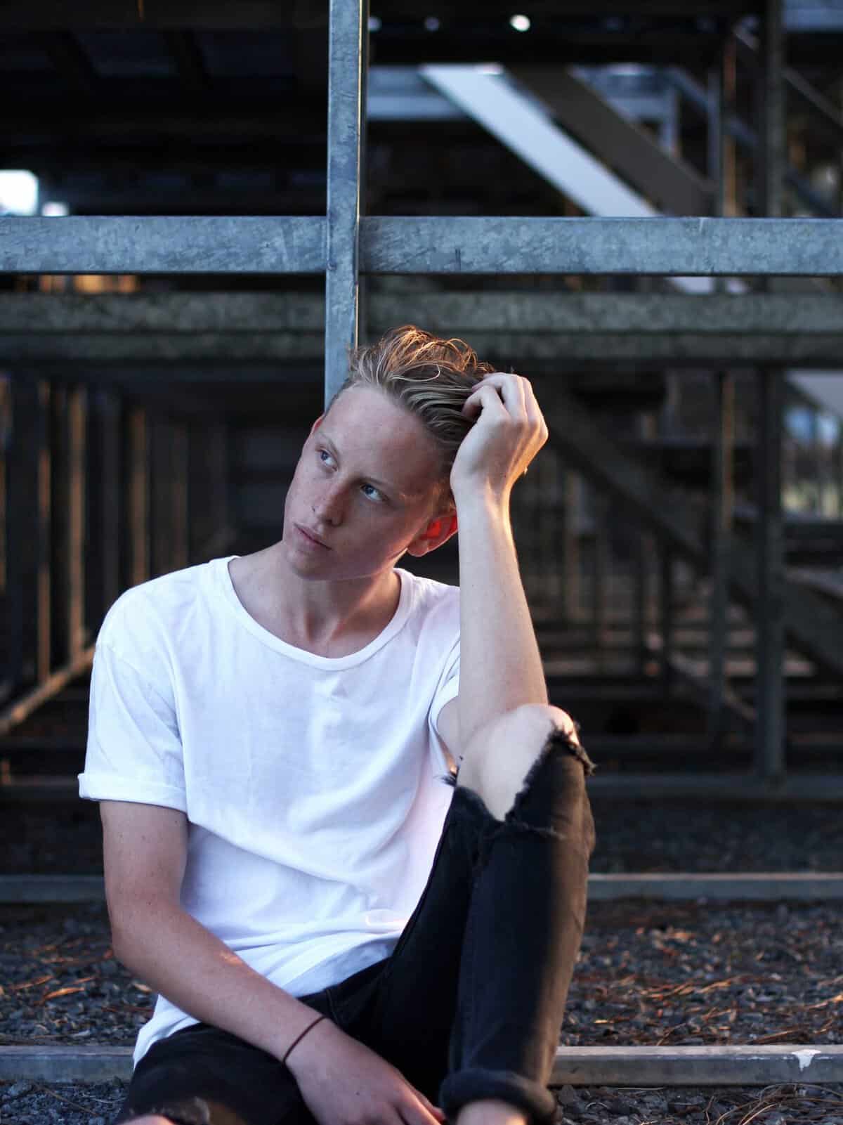 Young man sitting outside an industrial area staring off into the distance