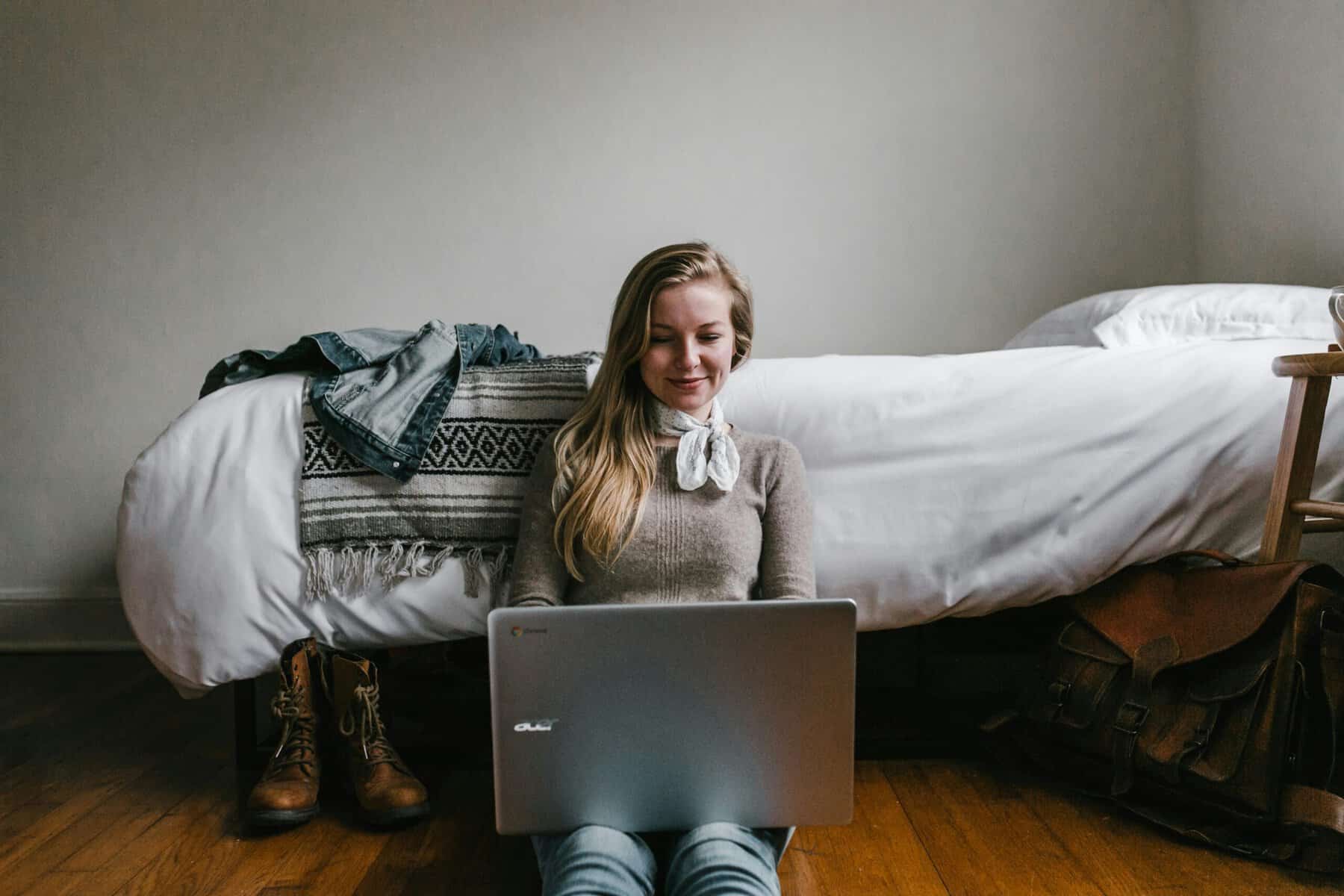Young woman sitting on the floor with a laptop, leaning back against her bed, researching autoimmune health information