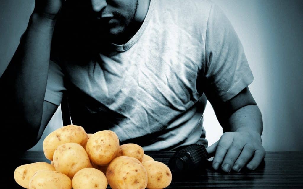Fresh potatoes on a wooden table with a man working in the background.