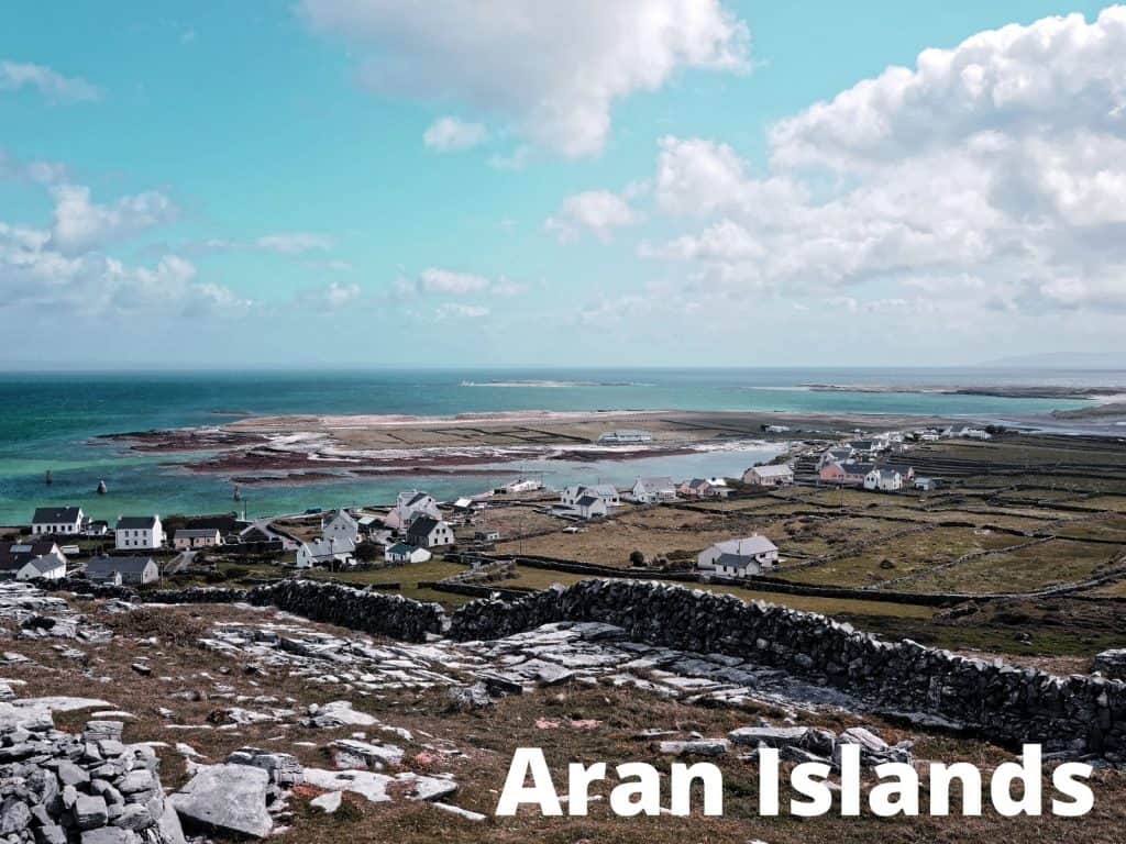 Seaside view of Aran Islands with white cottages, rocky landscape, and blue ocean under a partly cloudy sky.