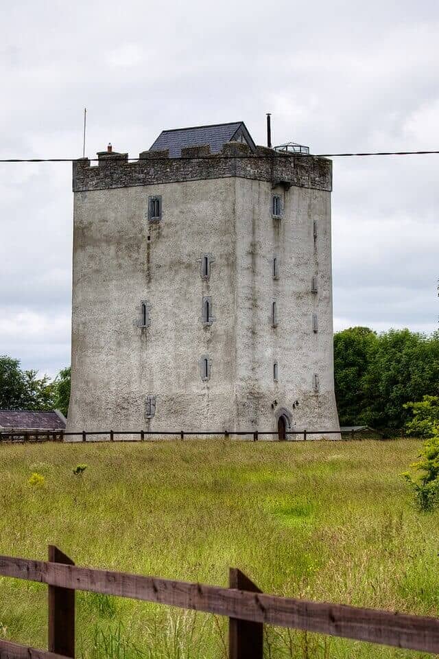 Weathered stone tower with small narrow windows in Irish countryside.