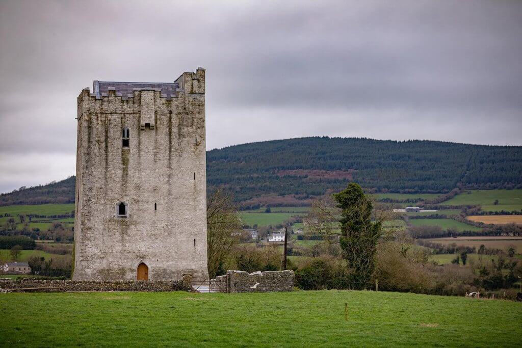 Medieval Irish tower castle with lush green landscape and rolling hills in the background.