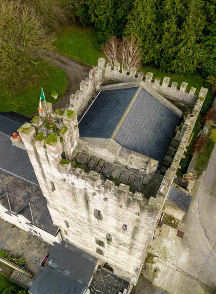 Aerial view of an ancient Irish castle with fortified walls and lush surrounding greenery.