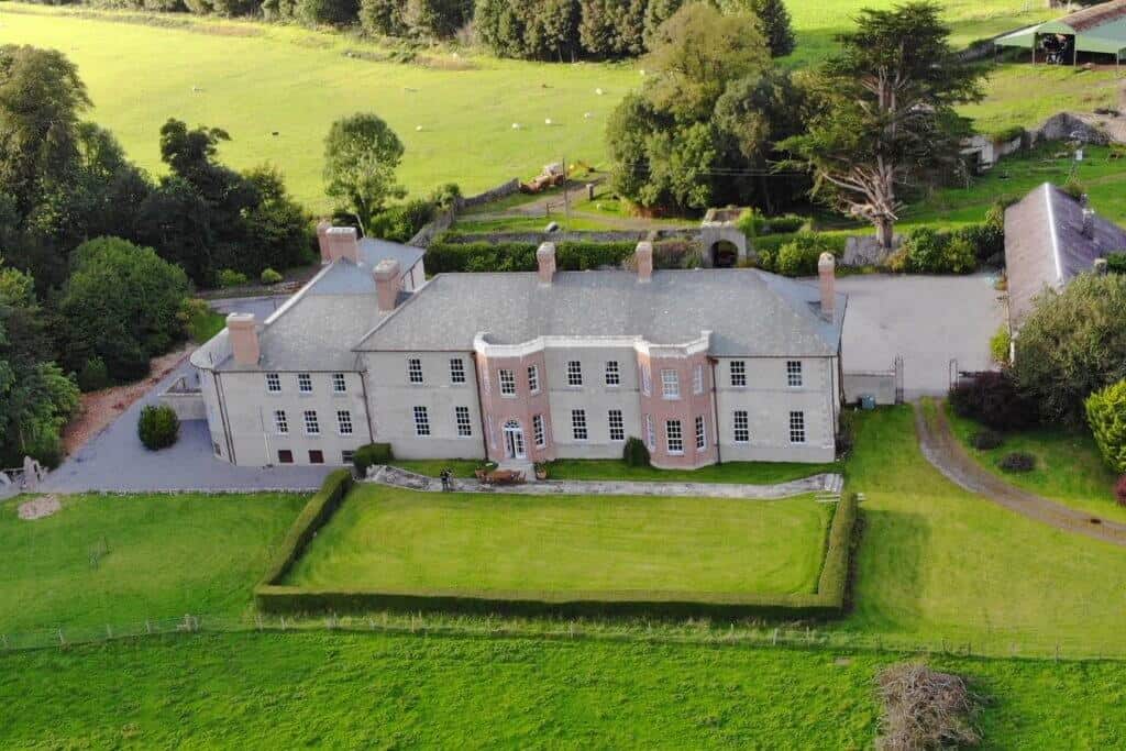 Historic Irish manor surrounded by lush green gardens and rolling countryside.