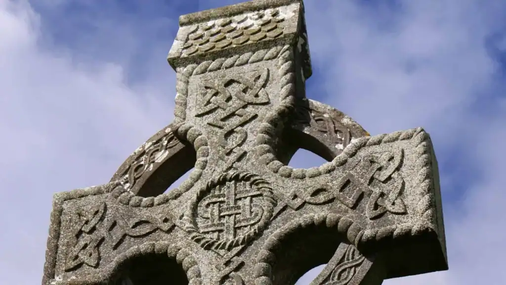Carved stone Celtic cross covered in Celtic knots and symbols against a blue sky
