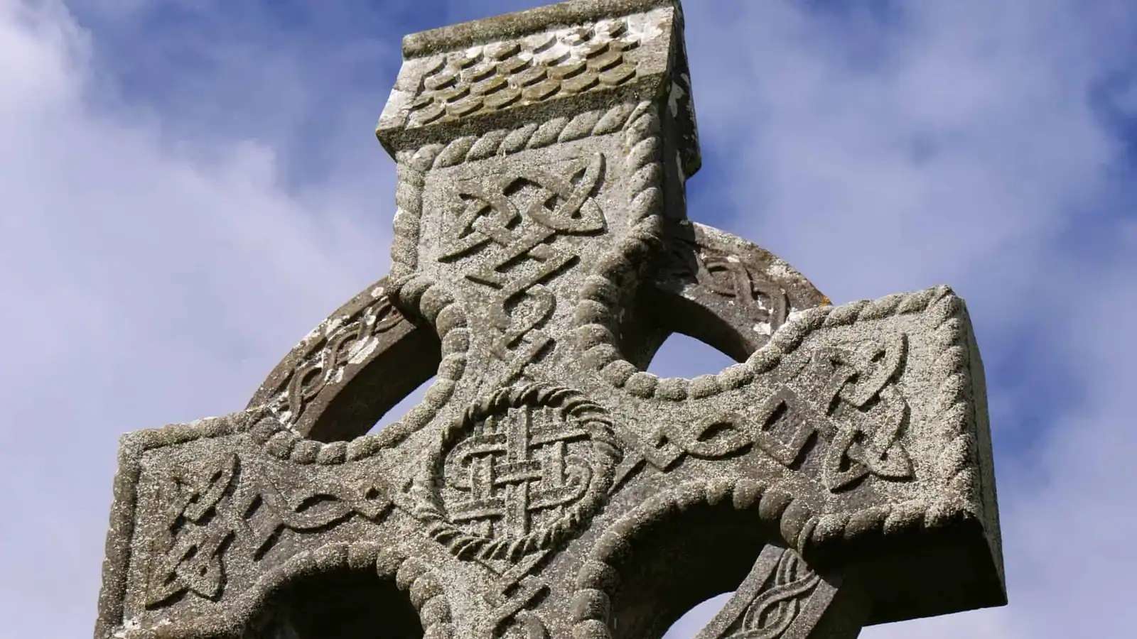 Carved stone Celtic cross covered in Celtic knots and symbols against a blue sky