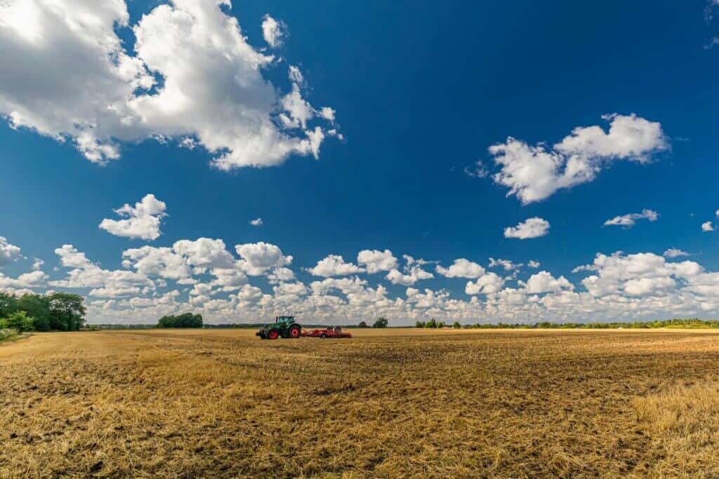 Vast Irish farmland under a bright blue sky with scattered clouds, featuring a tractor working the fields.