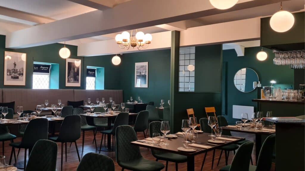 Elegant restaurant interior with dark green walls, ambient lighting, and neatly set tables.
