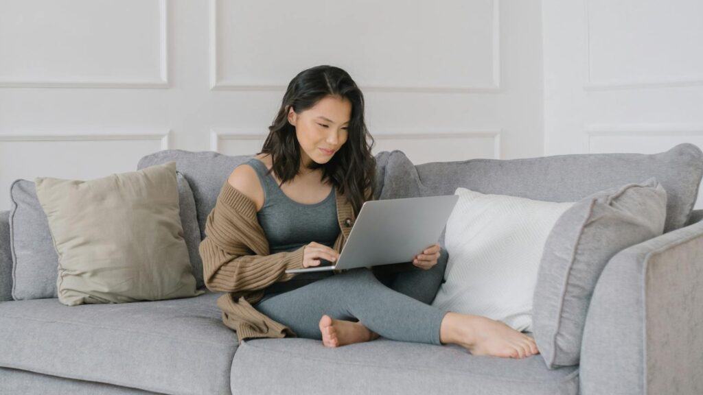Cozy woman browsing a laptop on a comfy gray sofa at home.