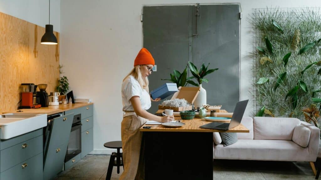 Cozy modern kitchen with a woman unpacking boxes while working on a laptop.