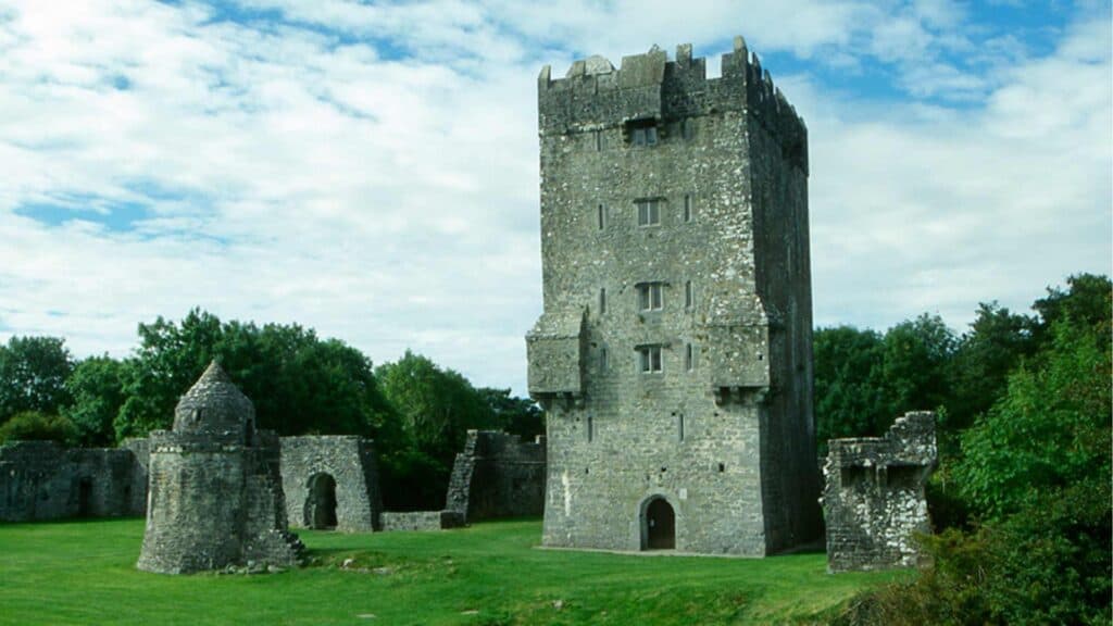 Ancient Irish castle tower surrounded by lush greenery under a cloudy sky.