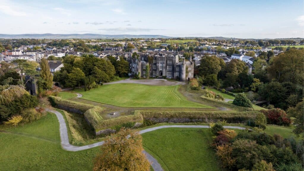 Historic Irish castle surrounded by lush gardens and scenic town views.
