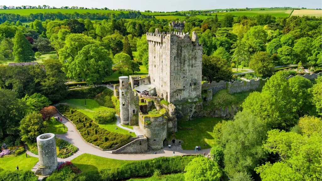 Aerial view of a historic Irish castle surrounded by lush green trees and vibrant gardens.