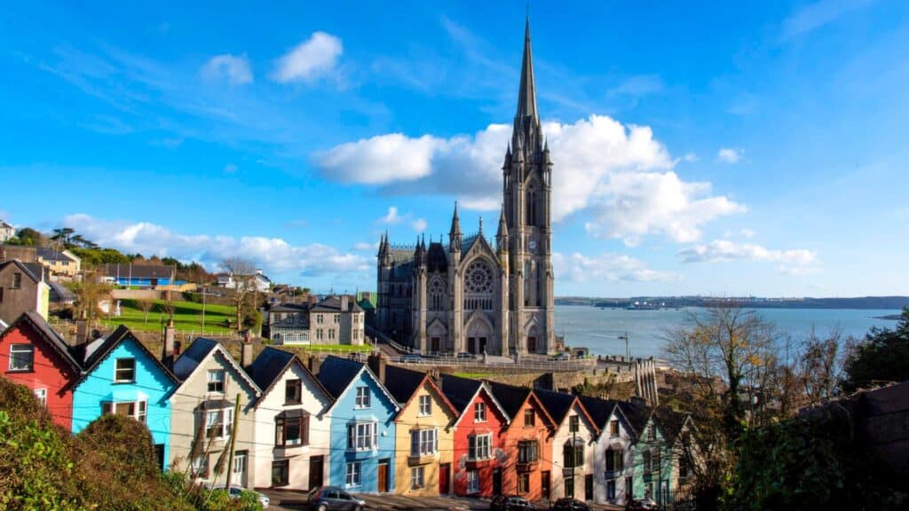 Colorful houses with a historic church and river in the background, showcasing Ireland's scenic coastal towns.