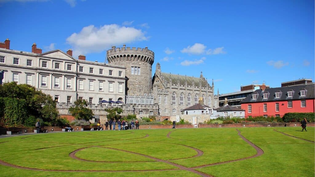 Bright blue sky and historiccastle ruins overlooking a lush green park in Ireland.