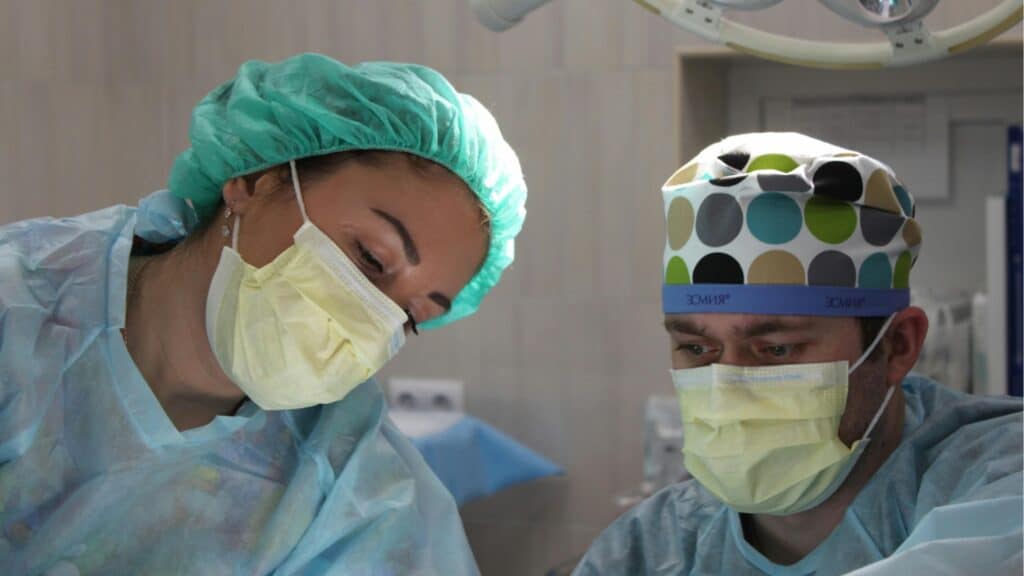 Surgical team performing a procedure in a hospital operating room, wearing protective masks and caps.