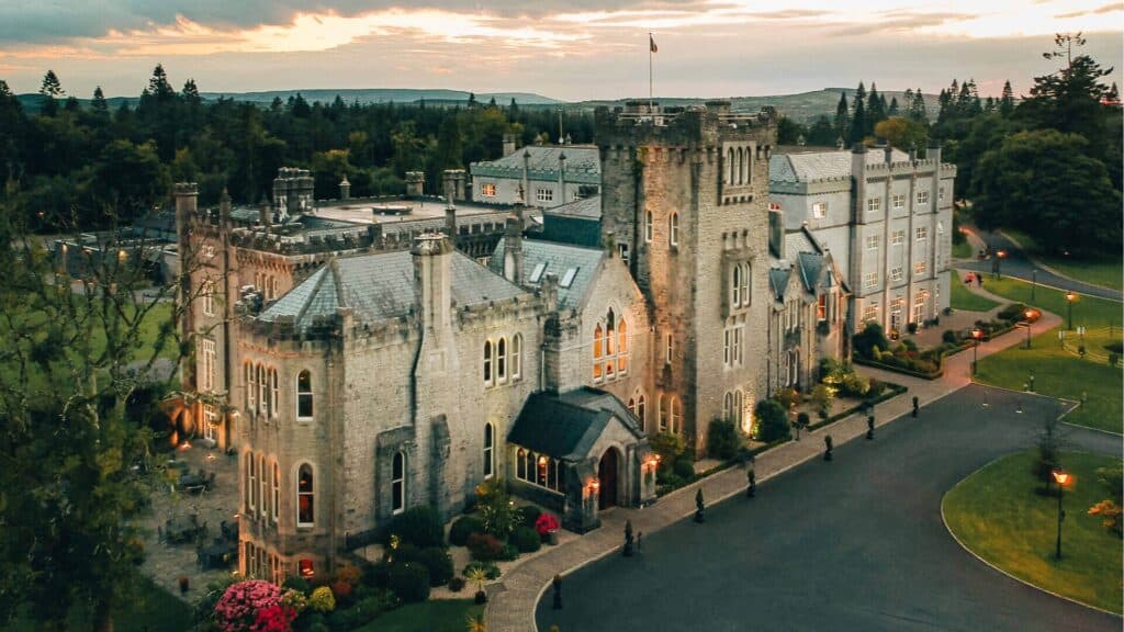Majestic Irish castle illuminated at dusk surrounded by lush greenery.