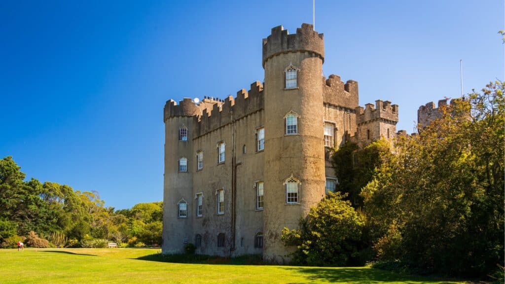 Ancient Irish castle surrounded by lush greenery under a bright blue sky.