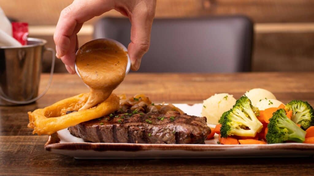 Juicy steak with gravy, served with season vegetables on a plate.