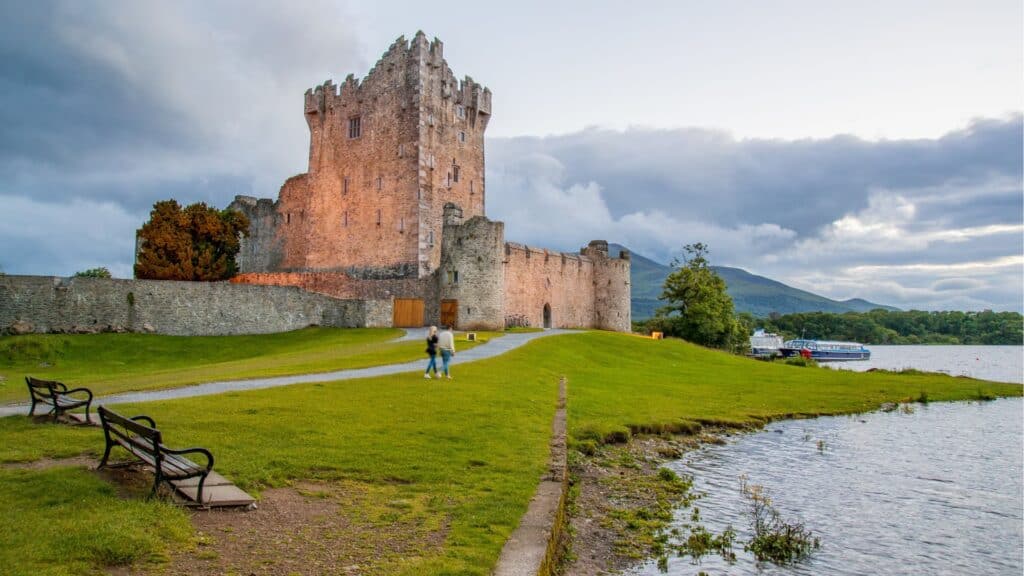 Majestic Irish castle by a lake with green lawns and mountains in the background.