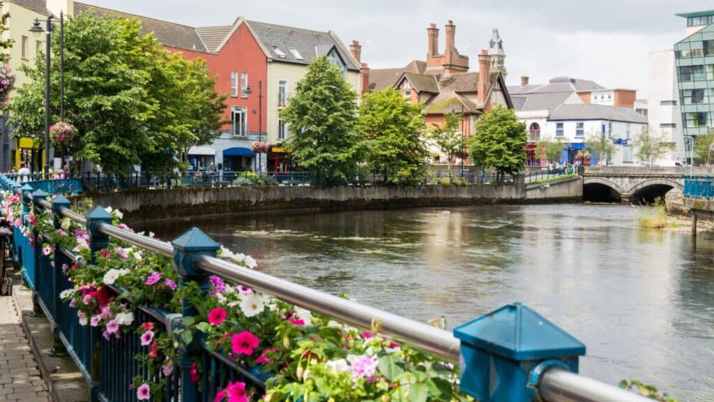Vibrant riverside scene in Ireland showcasing colorful houses and blooming flowers.
