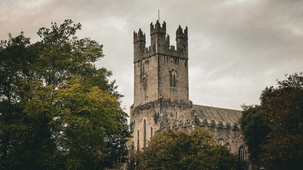 Ancient stone church tower surrounded by trees in Ireland.
