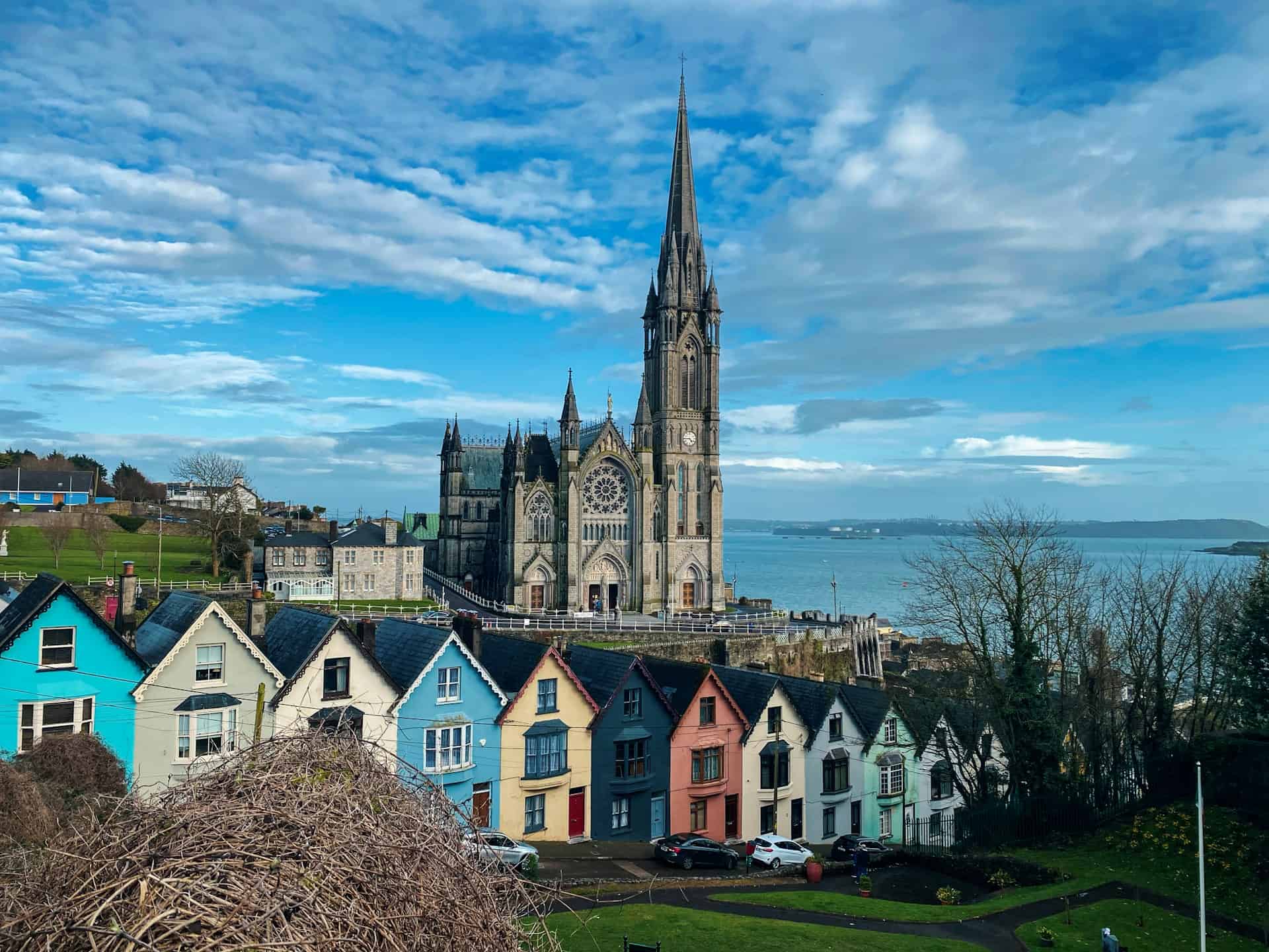 Colorful seaside houses near a historic stone church with a towering spire in Ireland.